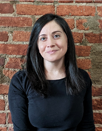 A women in a black shirt sits in front of a brick wall