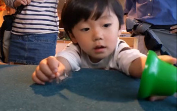 Young child at table reaching for plastic bell