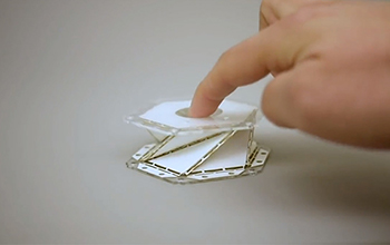 A hand testing the spring of a folded origami piece.